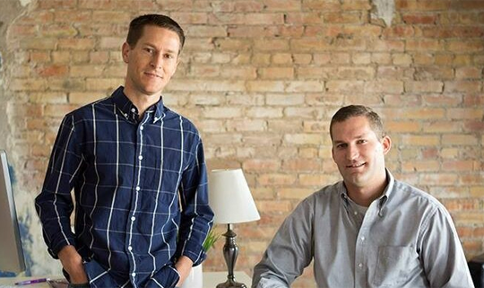 Two men in casual shirts standing in brick loft space