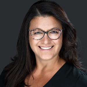 Woman with long dark hair wearing glasses smiling against gray background
