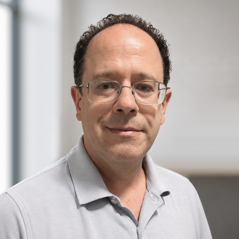 alan3 Professional headshot of man wearing light blue shirt and glasses indoors.